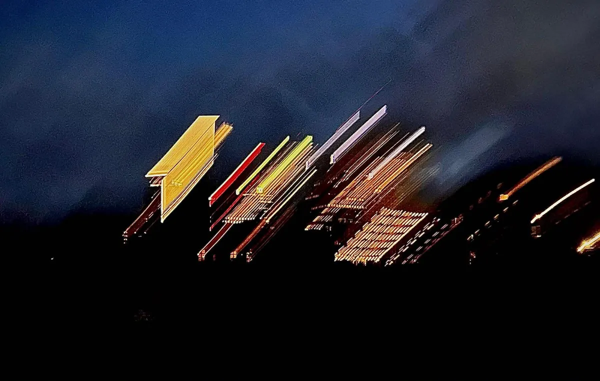 A long-exposure photograph of a lit building at night, its windows smeared into diagonal streaks of yellow, red and green.